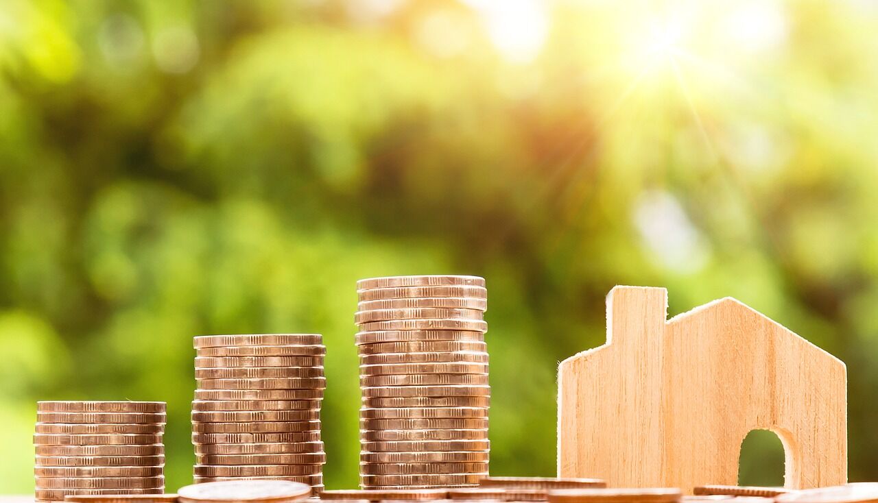 pile of coins along side a little wooden house